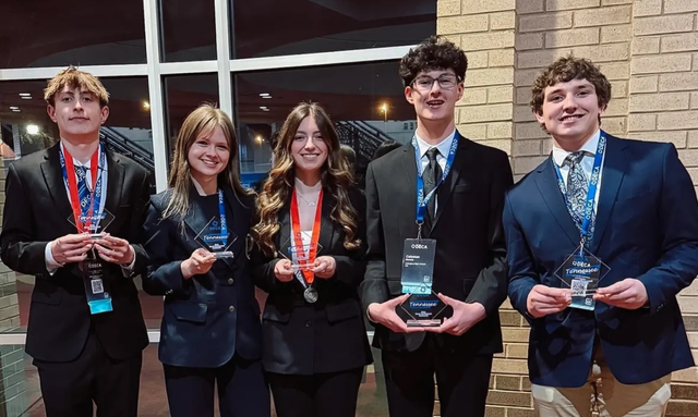 Arlington DECA chapter’s winners Noah Manthe (far left), Ashlynn Harrahill (left), Savannah Reynolds (middle), Coleman Dorsey (right), and Sawyer Oselies (far right) posing for a picture with their glass (DECA’s version of a trophy).